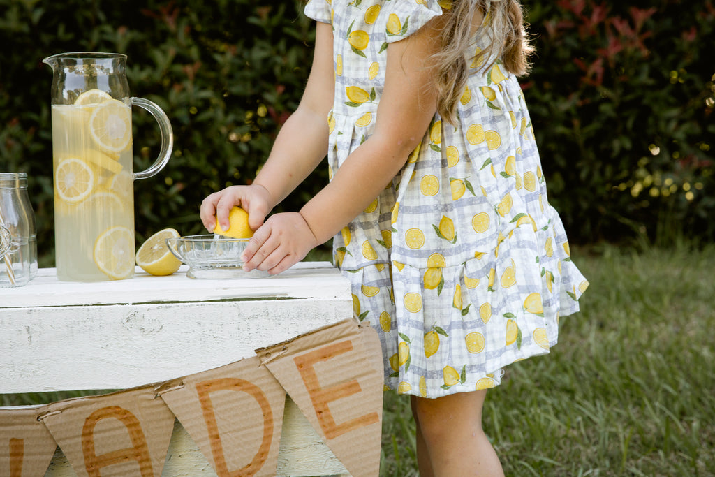 Lemonade print - a textured white linen base with a blue gingham and hand-drawn lemons. Handmade into a tiered skirt dress with frill cap sleeves. Handmade into short leg, rolled hem slouch cut overalls with tie top adjustable straps.