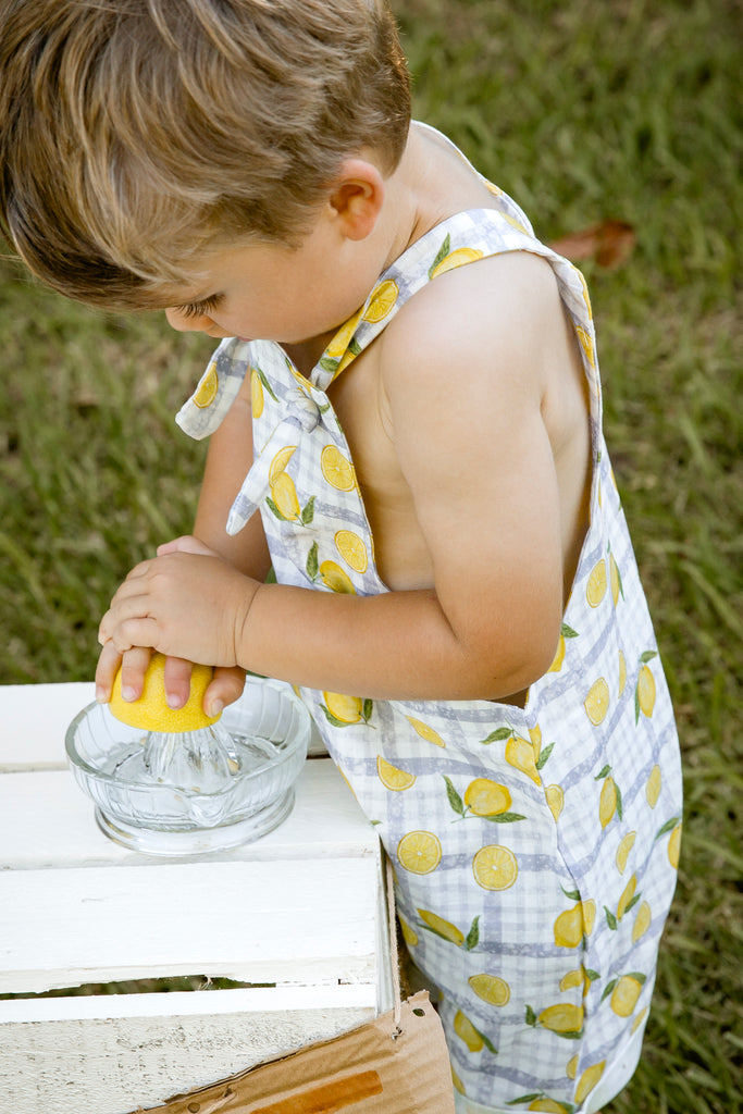 Lemonade print - a textured white linen base with a blue gingham and hand-drawn lemons. Handmade into short leg, rolled hem slouch cut overalls with tie top adjustable straps. Kids making lemonade at a roadside stand. Australian made.