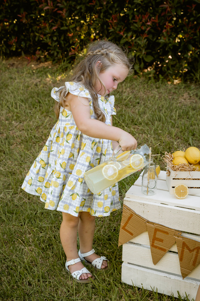 Lemonade print - a textured white linen base with a blue gingham and hand-drawn lemons. Handmade into a tiered skirt dress with frill cap sleeves.
