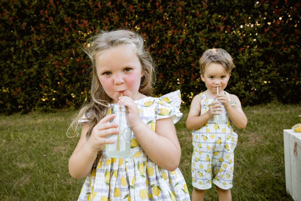 Lemonade print - a textured white linen base with a blue gingham and hand-drawn lemons. Handmade into a tiered skirt dress with frill cap sleeves. Handmade into short leg, rolled hem slouch cut overalls with tie top adjustable straps.