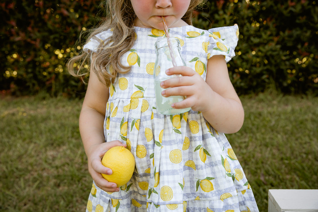 Lemonade print - a textured white linen base with a blue gingham and hand-drawn lemons. Handmade into a tiered skirt dress with frill cap sleeves.