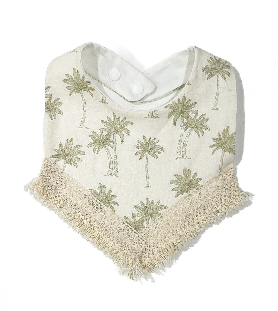 Palms and ecru / off-white textured linen with subtle warm green palm tree print. Handcrafted into a children’s bib with a tassel edge and adjustable clip back.