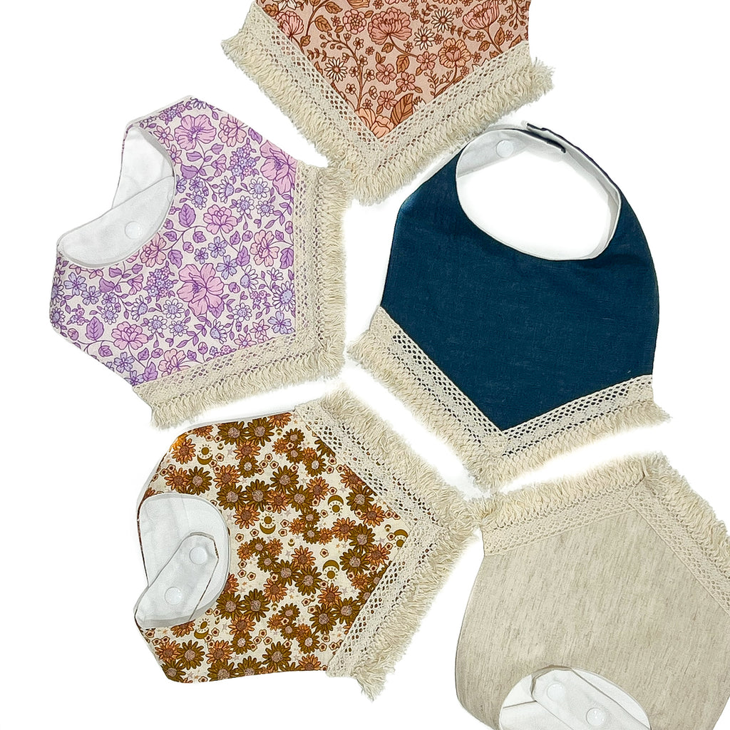 A collection of handmade children’s cotton bibs with a tassel edge and clip back.