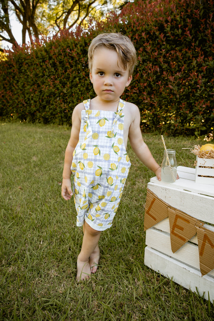 Lemonade print - a textured white linen base with a blue gingham and hand-drawn lemons. Handmade into short leg, rolled hem slouch cut overalls with tie top adjustable straps. Kids making lemonade at a roadside stand. Australian-made.